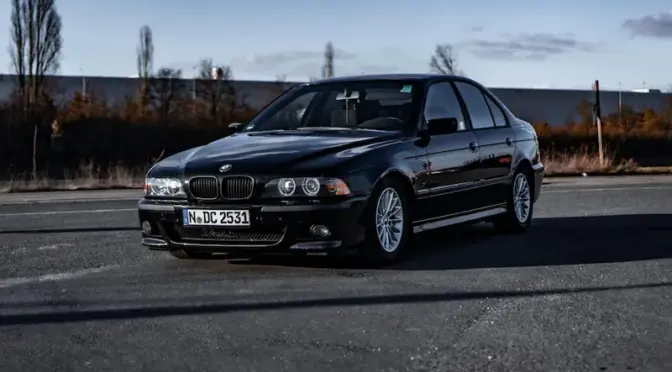 Czarne BMW E39 Sedan na klasycznych wieloramiennych felgach, widok z boku na asfalcie.