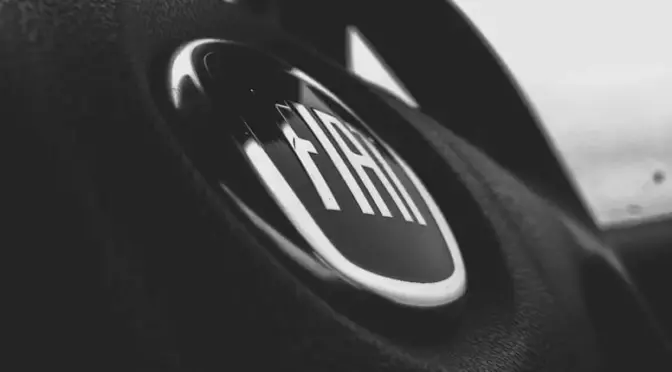 Zbliżenie w skali szarości na logo Fiat na kierownicy samochodu, artystyczne ujęcie wnętrza.